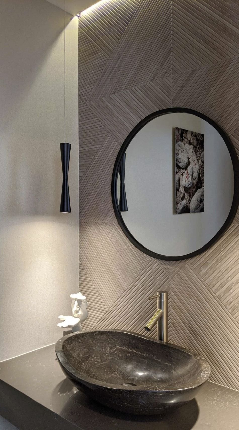 A powder room with a stone vessel sink and slim black sconces on herringbone tile