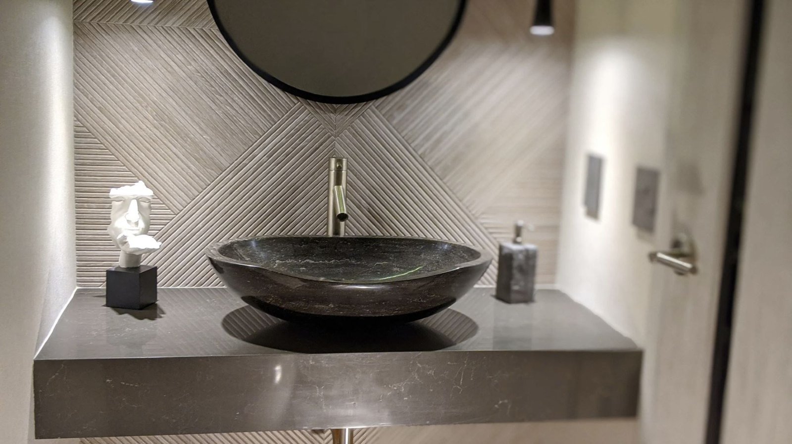 A carved stone vessel sink on a floating concrete vanity beneath a round black mirror