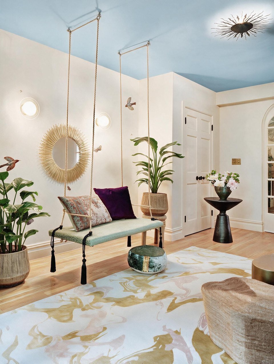 Hanging rattan swing seats over a gold-and-white rug beneath a sky-blue ceiling