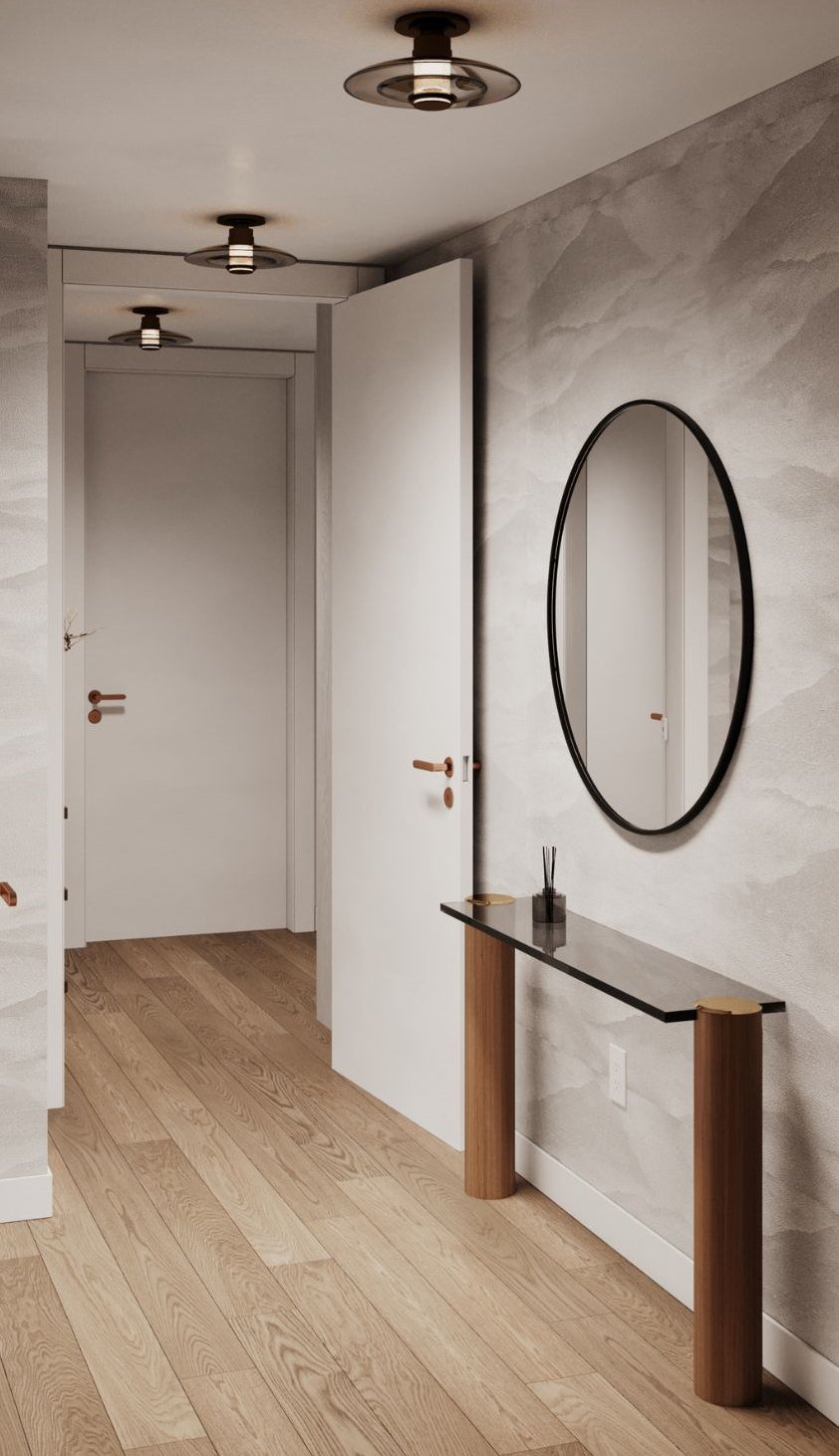A hallway with a marble wall, round mirror and slim console