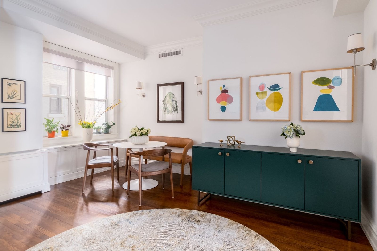 An Upper West Side dining room with a round table, walnut chairs and a green sideboard below a trio of prints