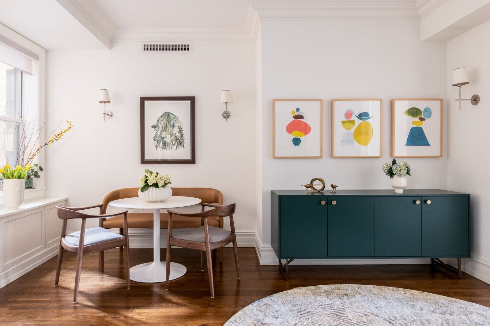 A round dining table and cane chairs beside a deep teal sideboard