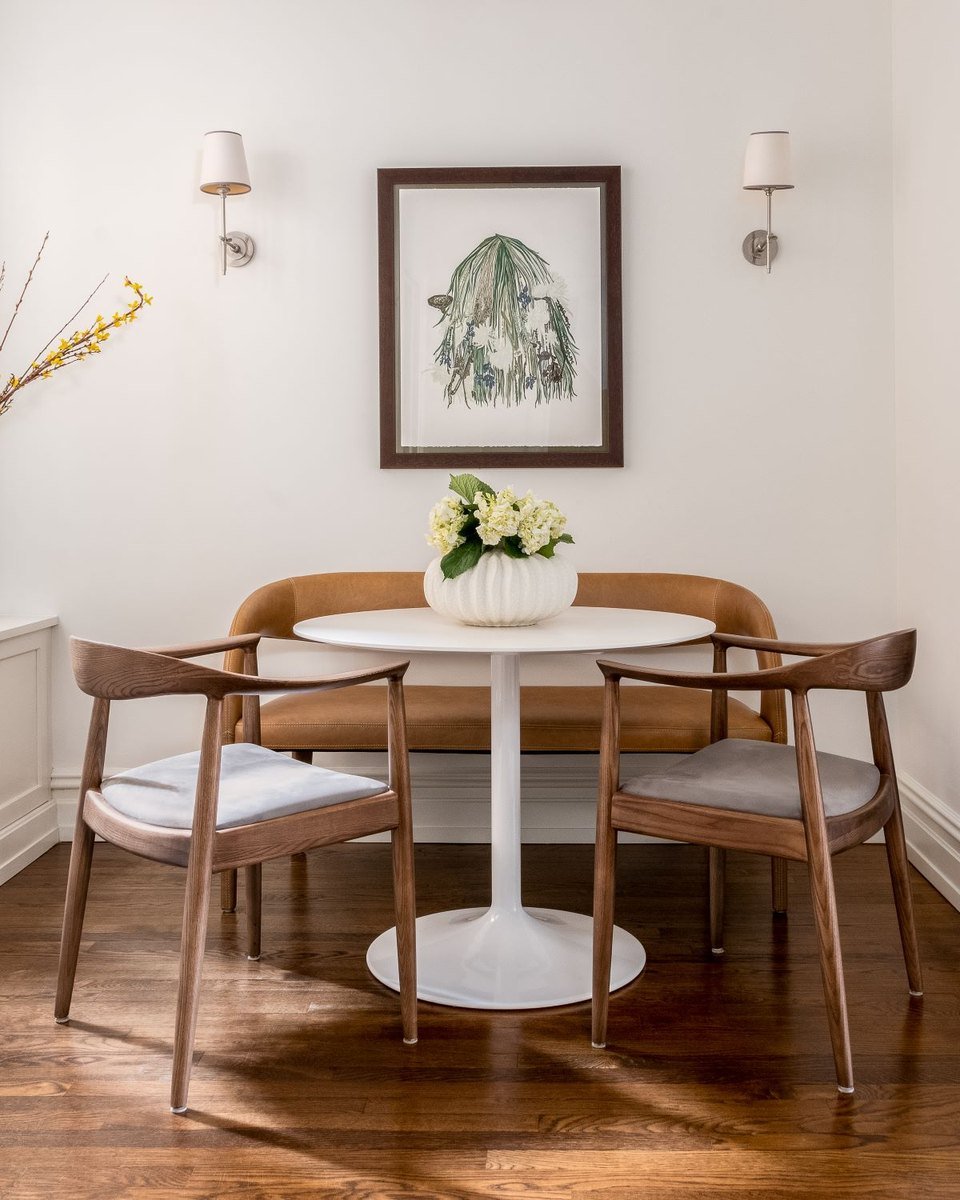 A round dining table with cane chairs beneath a framed print