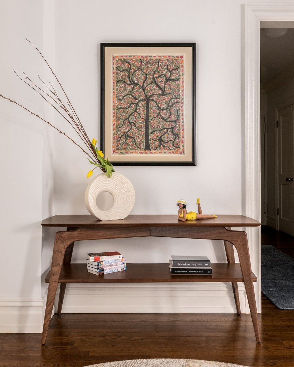 A walnut console table with a ceramic vase and artwork above