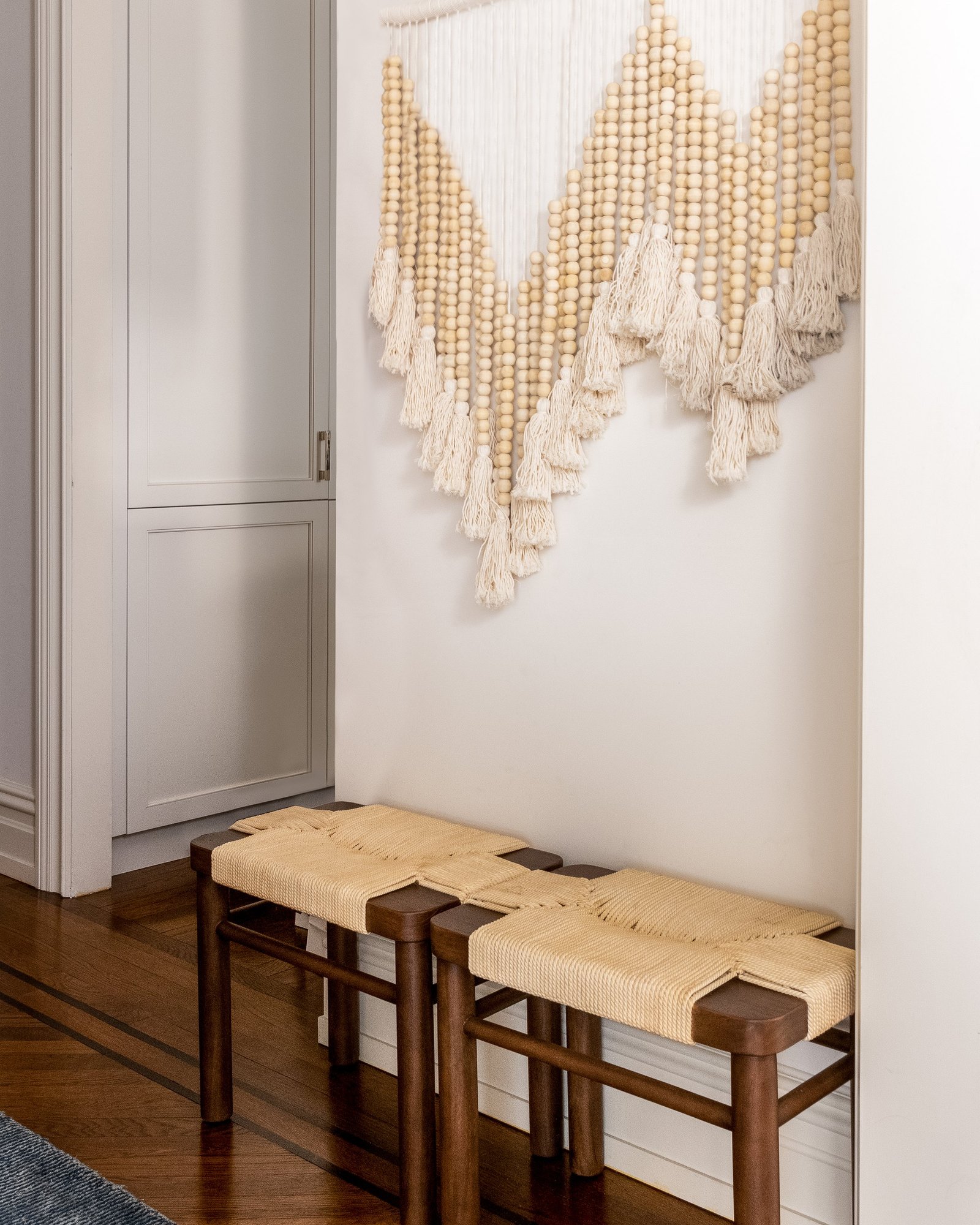 Two woven wood benches beneath a large macramé wall hanging in a prewar hallway