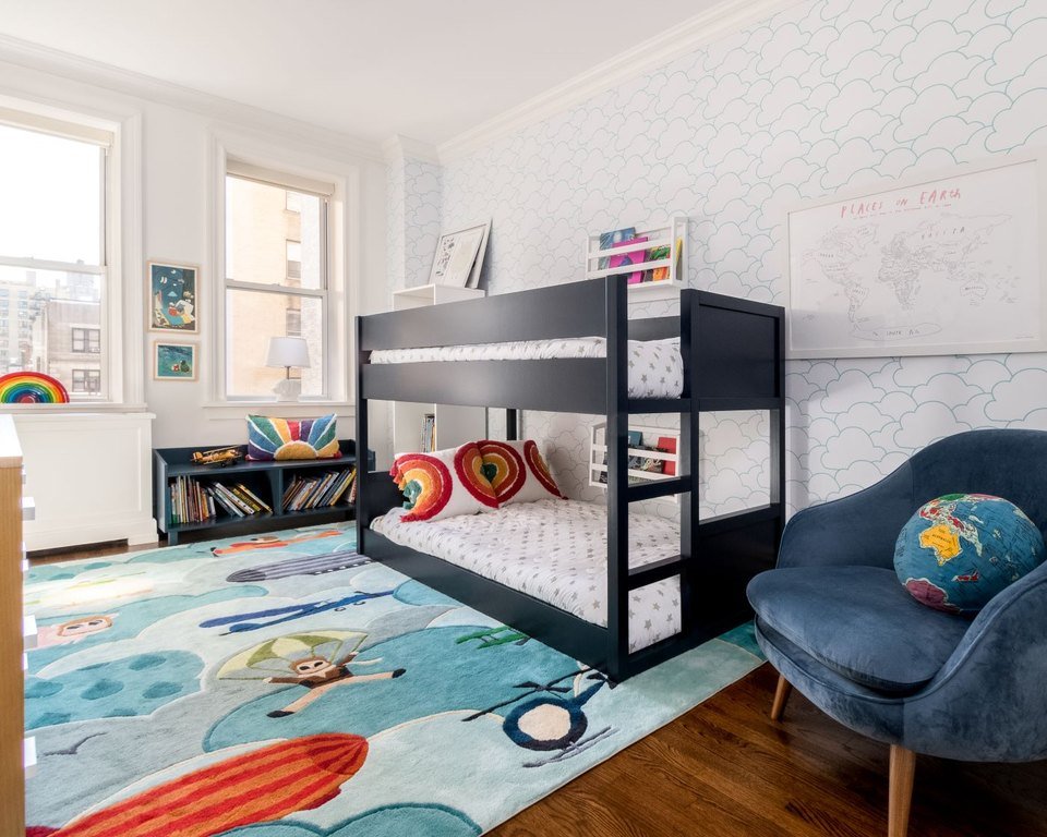 A children's room with bunk beds, a blue armchair and a rainbow rug