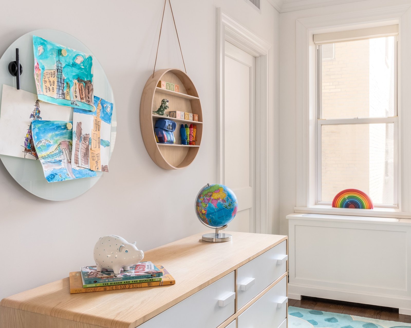 A round wall shelf and circular pinboard above a white and oak desk in a child's room