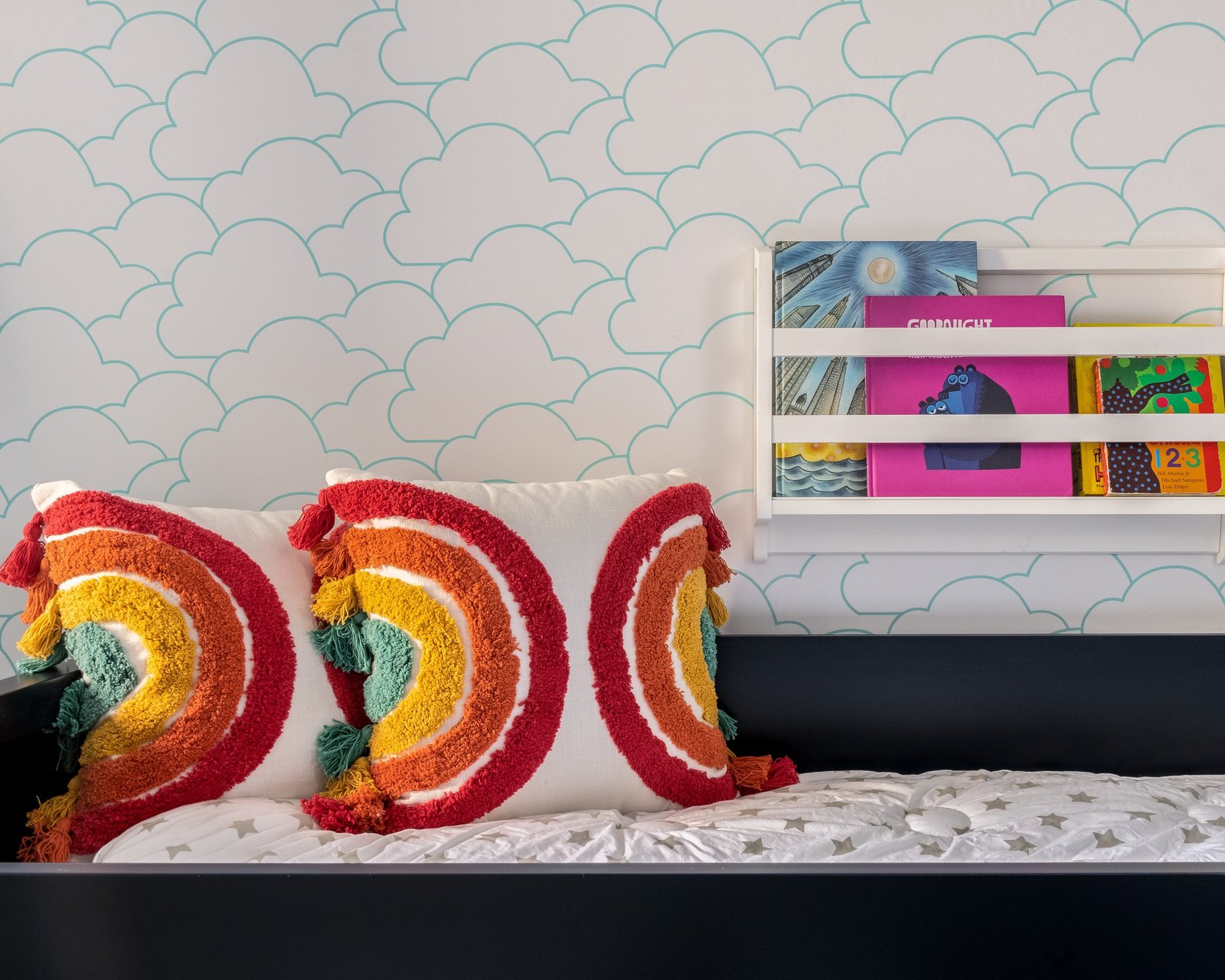 A navy window daybed with rainbow cushions below a wall-mounted book rack in an Upper West Side kids' room