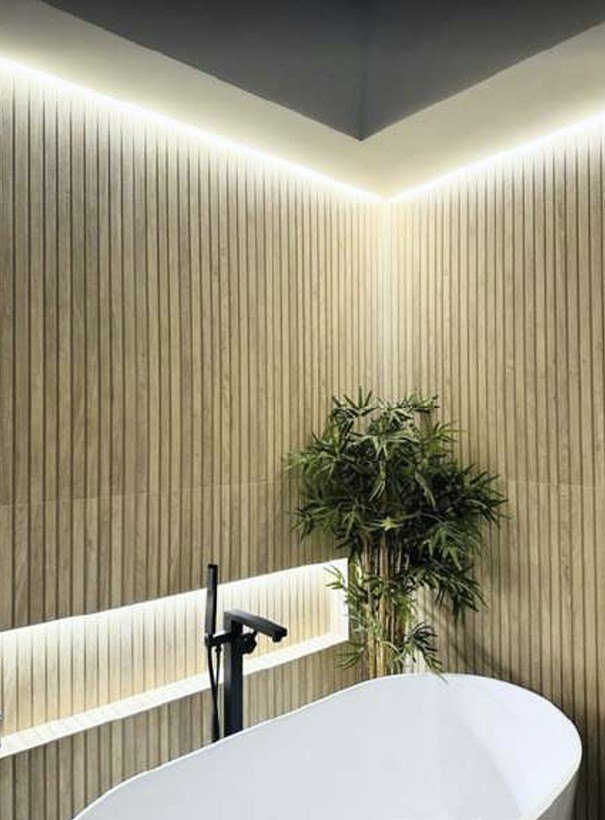 A cove-lit slatted oak wall behind a freestanding tub