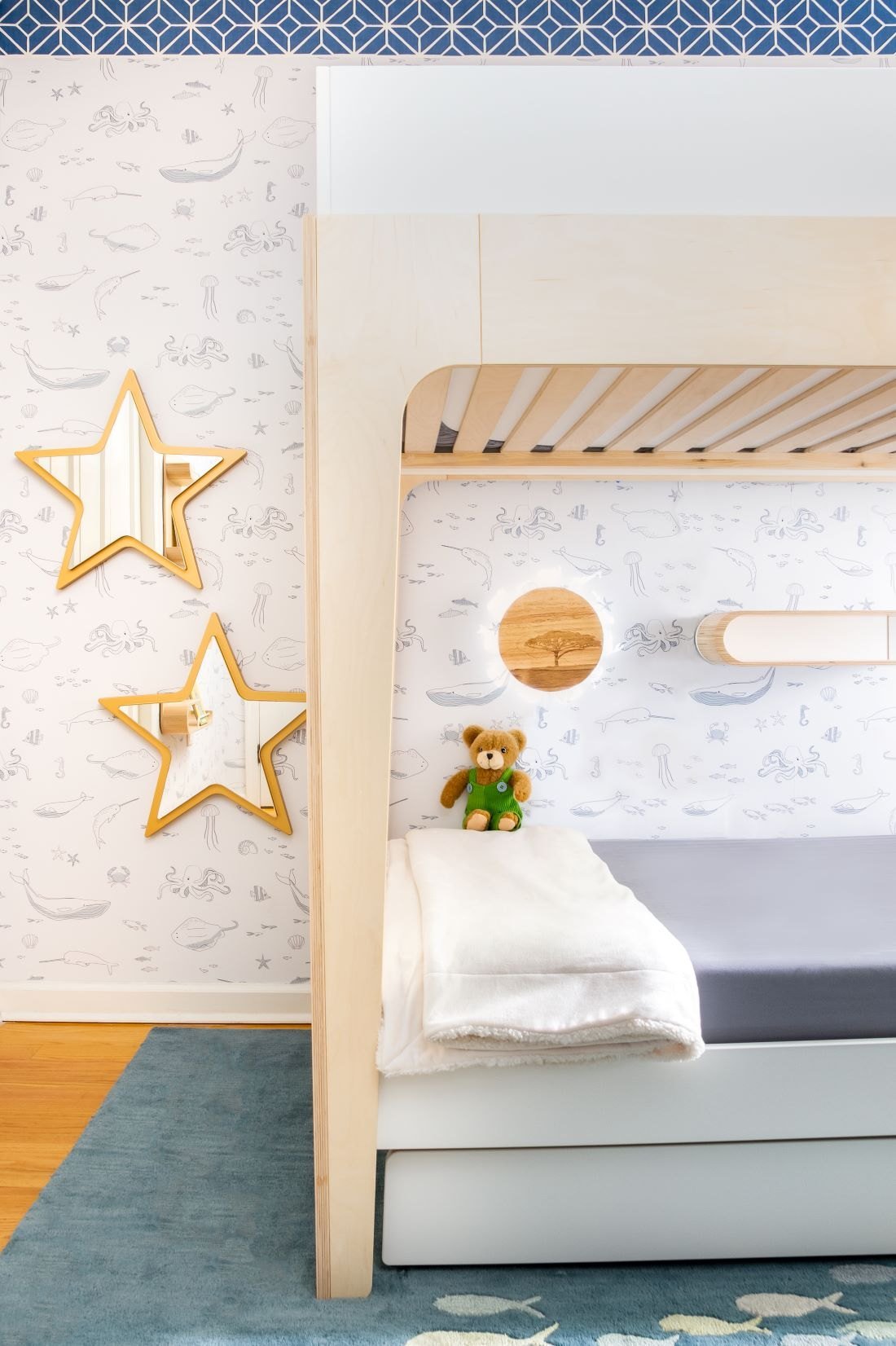 A birch bunk bed with a built-in reading light and gold star wall lights against cloud wallpaper