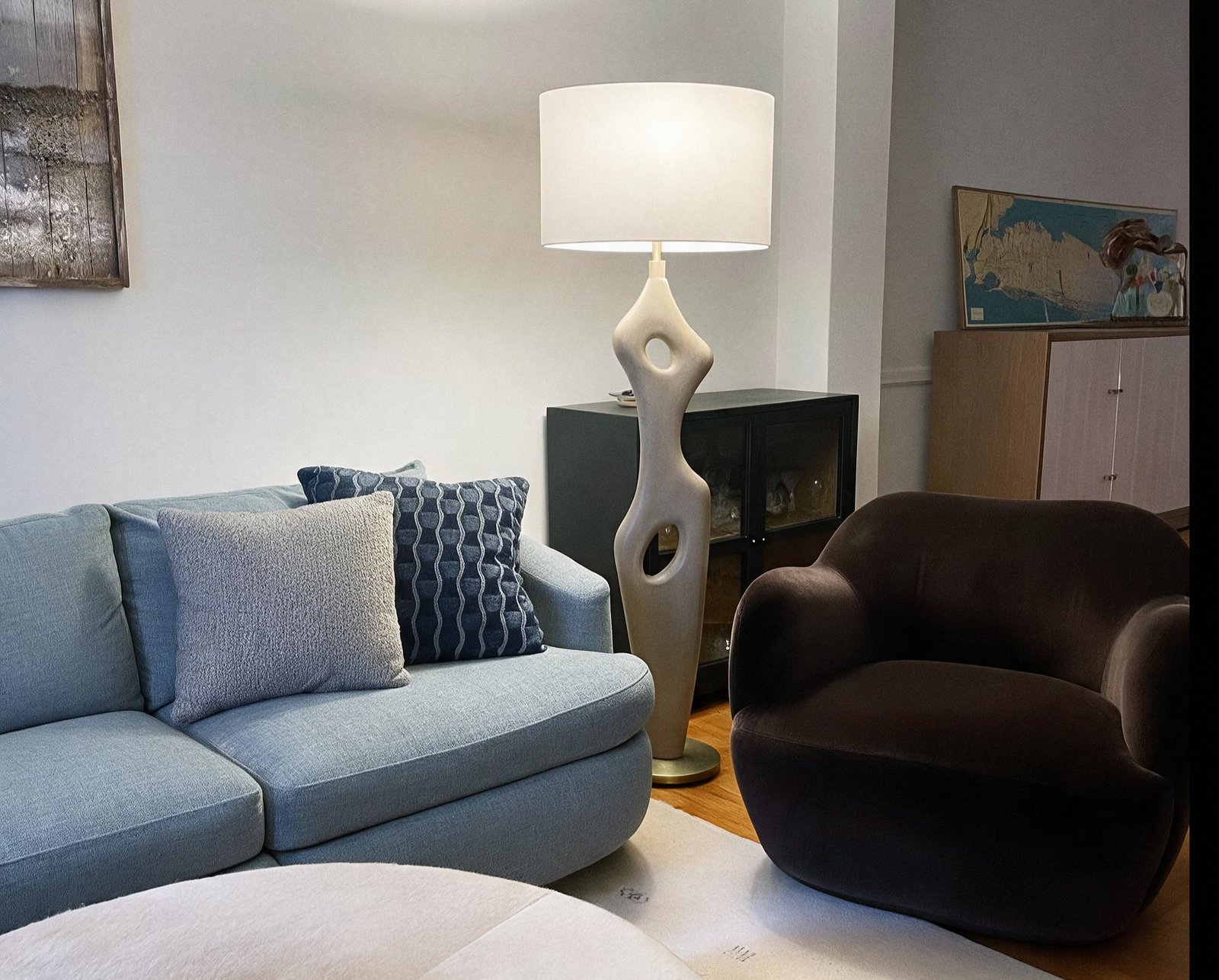 A sculptural cream floor lamp between a blue linen sofa and a deep brown bouclé armchair