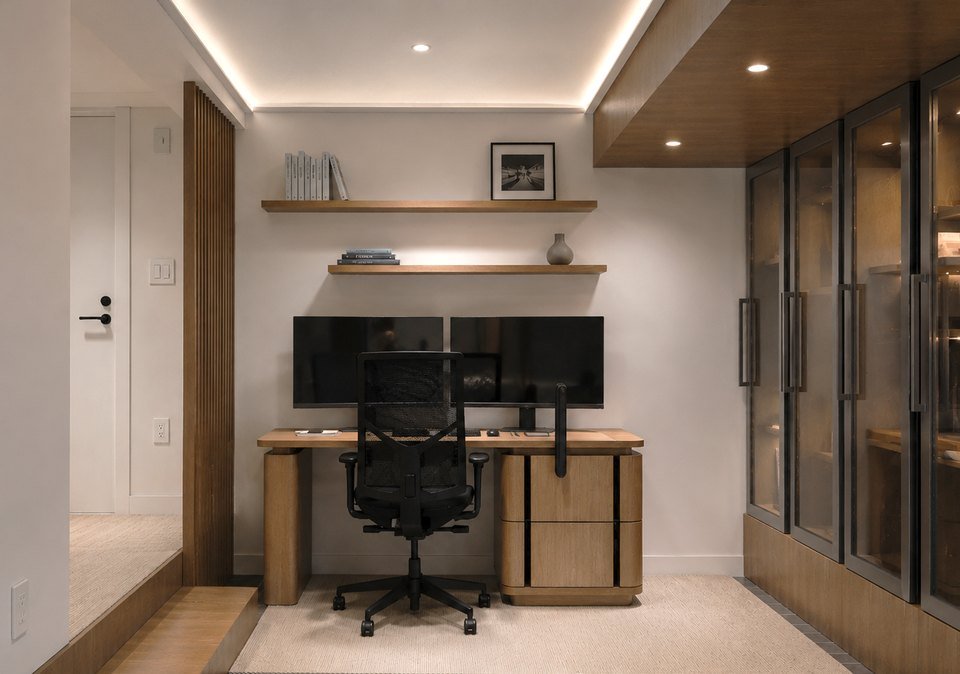 A built-in desk with dual monitors and glass-front cabinetry